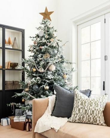 witte woonkamer met grote Scandinavische kerstboom met veel speelgoed, bank met kussens