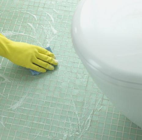 Käsi kummikinnas vannitoas plaaditud põranda puhastamisel