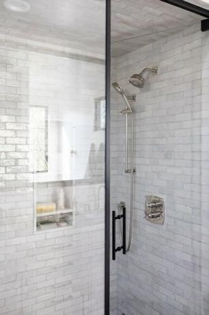 Stiklinės dušo durys su pilkomis plytelėmis išklotomis sienomis