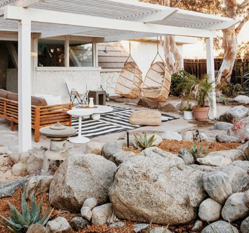 Witte houten moderne pergola met hangende stoelen, bank, buitendeken en rotstuin.