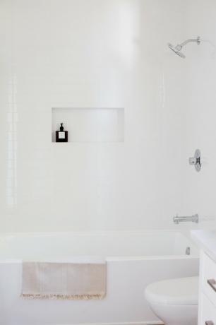 banheira branca com uma toalha com franjas estendida, parede de chuveiro branca