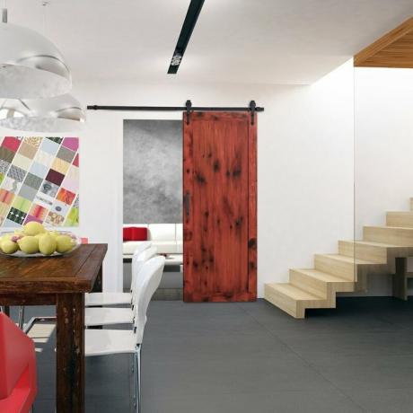 Portas de celeiro contemporâneas manchadas de vermelho, mesa de jantar rústica de madeira escura, cadeiras de jantar brancas, escada, luminárias pendentes de vidro.