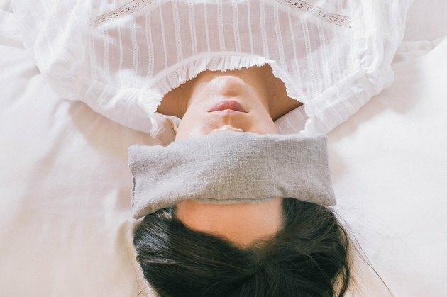Pessoa deitada na cama com almofada para os olhos
