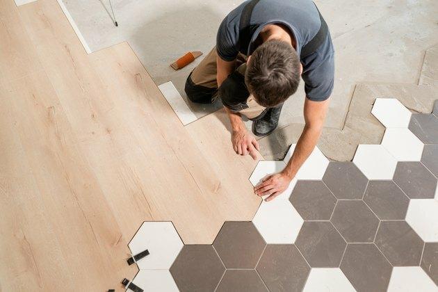 Meessoost töötaja paigaldab uue puitlaminaatpõranda. Laminaadi ja keraamiliste plaatide puitpaneelide kombinatsioon kärgstruktuuri kujul. Köögi renoveerimine.