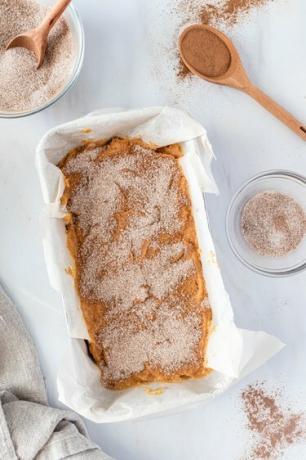 Una teglia foderata con carta da forno e riempita con la pastella condita con zucchero alla cannella.