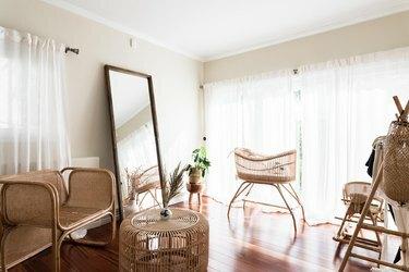 Vivaio boho minimalista con culla, sedia e tavolo in rattan. Uno specchio a figura intera, vedove dalle tende bianche e fiori secchi.