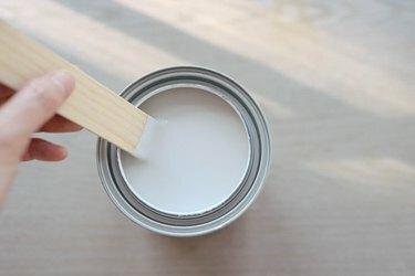 Persona che mescola una lattina di vernice al latte con un bastoncino di vernice