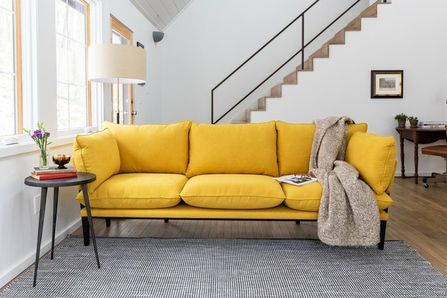geltona sofa prie laiptų su pilku kilimu ir šoniniu stalu