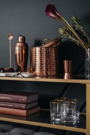 Prateleiras com livros e copos com conjunto de coquetel e flores de cobre
