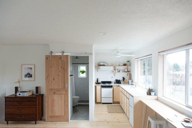 Portas de celeiro contemporâneas com vista completa do estúdio com paredes brancas, cômoda, porta do banheiro do celeiro, cozinha compacta com prateleiras abertas