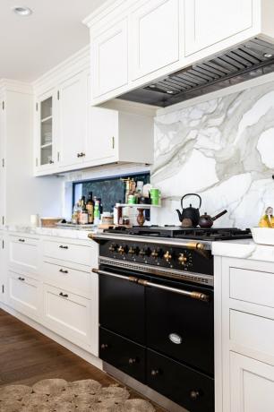 Uma cozinha com armários brancos, backsplash de mármore e piso de madeira