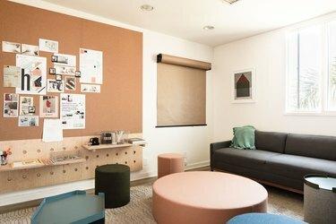 uma área de estar com um sofá cinza, grandes mesas redondas de centro e um rolo de papel pardo pendurado na parede