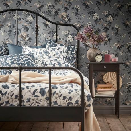 quarto com papel de parede floral e lençóis florais e mesa de cabeceira preta