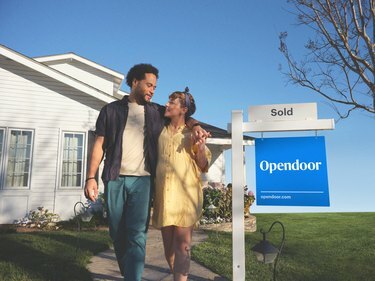 coppia sorridente a casa con opendoor venduto segno nel cortile