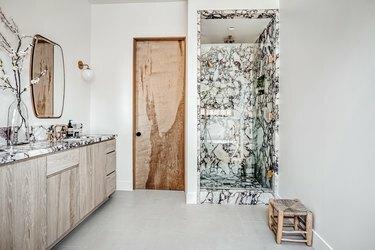 O baie cu duș de marmură, chiuvetă din lemn și ușă din lemn
