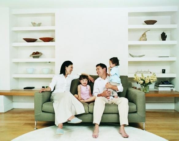 Šypsosi keturių asmenų šeima, sėdinti ant svetainės, esančios ant sofos