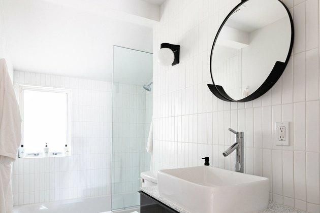 Um banheiro minimalista com azulejos brancos e um espelho redondo preto