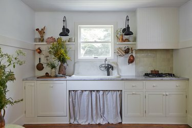 Hvidt bondekøkken med linnegardiner under vasken.
