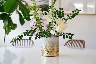 Tekstuuriga kuldvalge vaas roosade ja valgete lillede ja lehtedega