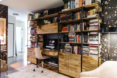 escritório doméstico escuro com uma parede de estantes de estilo industrial cheias de livros