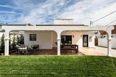 O curte de casă în stil spaniol, cu o verandă acoperită și o peluză verde luxuriantă