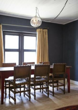 Una sala da pranzo con pareti blu scuro con sala da pranzo in legno e lampada a sospensione a globo