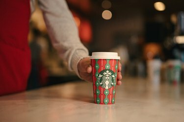 henkilö, joka asettaa puna-vihreän starbucks-kupin pöydälle