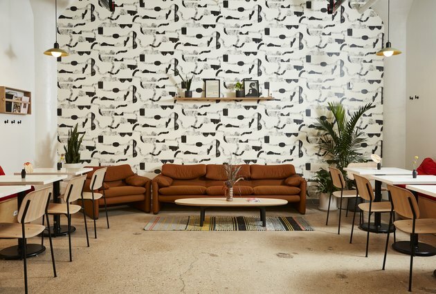 zonă de relaxare cu tapet grafic alb-negru, canapea maro, scaune și mese din lemn ușor