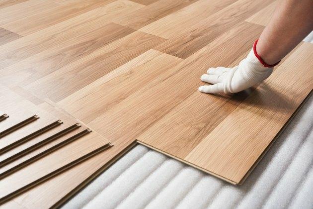 Installazione di pavimento laminato, dettaglio sulla mano dell'uomo in guanto bianco con piastrella in legno, su strato di base di schiuma bianca