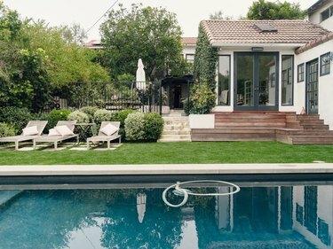 O casă albă cu trepte care duc în curtea din spate; o piscină interioară înconjurată de o peluză verde