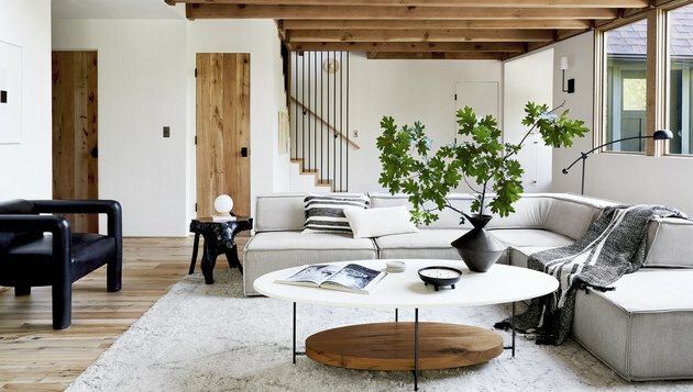 midcentury تصميم غرفة عائلية حديثة من إميلي هندرسون مع طاولة جانبية من الخشب الطبيعي وأريكة رمادية على شكل حرف L.