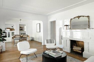 Minimalistinė ir šiuolaikiška svetainė su baltais ir juodais baldais bei neutraliais, medžio akcentais.
