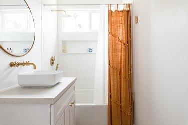 Et minimalistisk hvidmuret badeværelse med en hvid forfængelighed og guldorange accenter