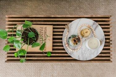 Inspirowany średniowieczem stolik z drewnianych listew z ozdobną książką, rośliną doniczkową i talerzem ze świecami na beżowym dywanie