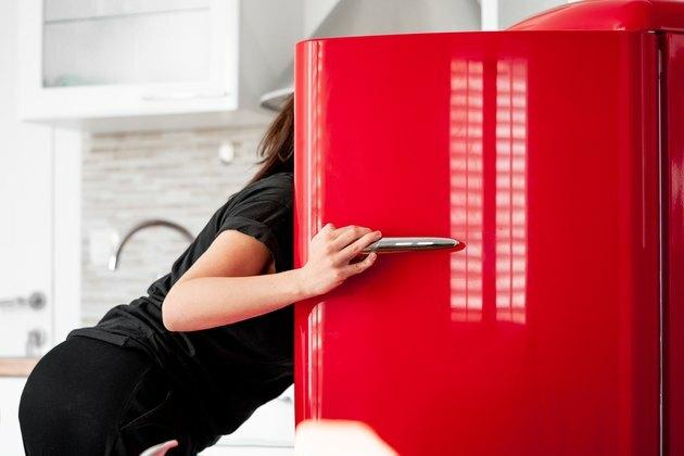 Mujer buscando comida en el refrigerador en modernos apartamentos luminosos.