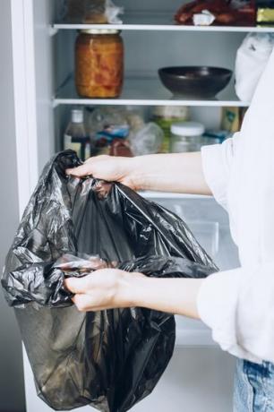 Käsi musta roskapussi täysin varustetun valkoisen jääkaapin edessä