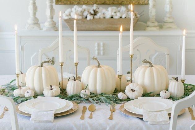 DIY herfst decor idee met witte pompoen middelpunt op witte tafellaken tafel met taps toelopende kaarsen