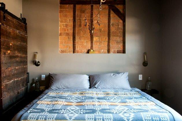 industriële boerderij bed met een blauwe sprei in een kamer met een muur zijdelings met houten planken en een in gipsplaat met een uitgesneden bakstenen