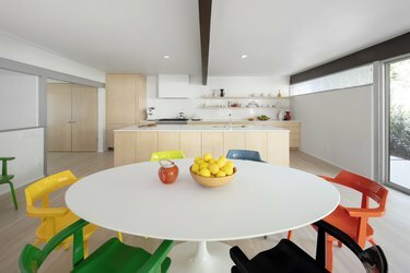 interno di una casa con zona cucina, tavolo bianco e sedie colorate