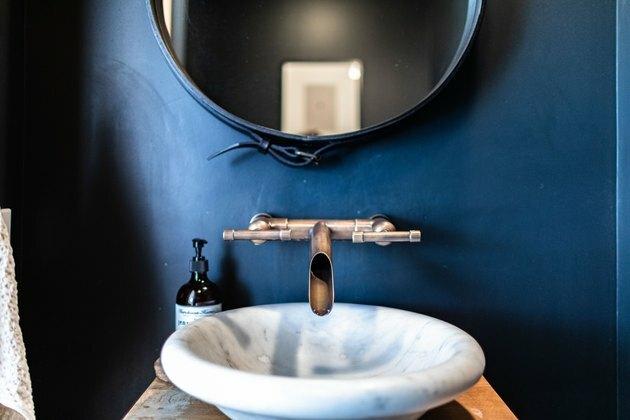 lavabo a vaso in pietra con rubinetto a parete, pareti blu scuro, specchio rotondo