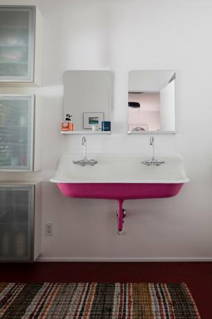 chiuveta din fonta roz, montata pe perete, cu interior alb, robinete duble argintii, doua oglinzi dreptunghiulare, covor zona multicolor, trei dulapuri de depozitare încorporate clare