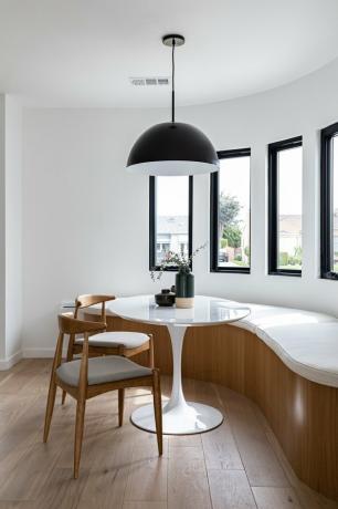 design de casa ecologicamente correto com sala de jantar curva contemporânea com banco curvo, mesa redonda pequena, cadeiras, luminária pendente e janelas altas