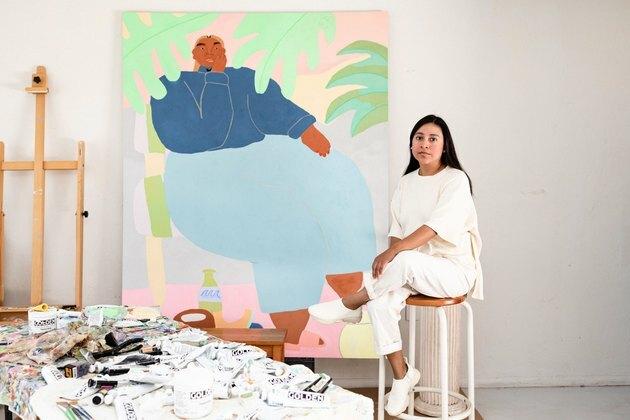 nő ül a széken, nagy festmény közelében