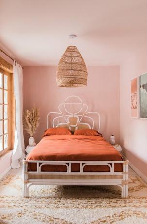 Zonsondergangkleurige roze slaapkamer met geweven bohemien hanger en bedframe van rotan