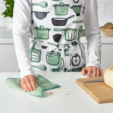 pessoa com avental segurando um pano de prato verde perto da tábua com pão