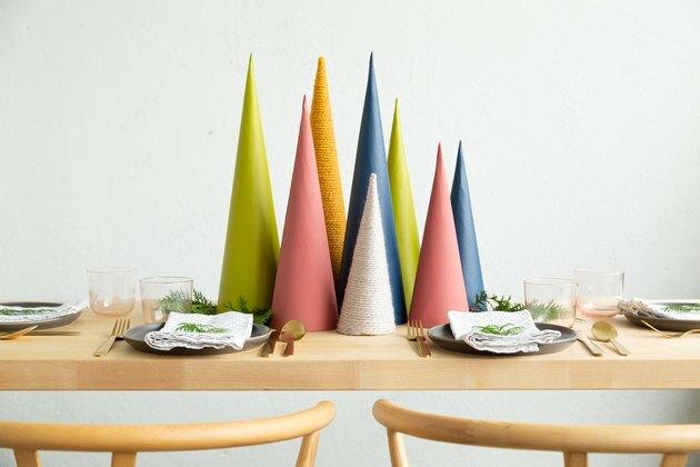 Ideia de decoração de Natal com uma peça central de feriado DIY feita de cones de papelão coloridos, ramos de folhagens e neve falsa
