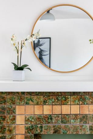 Uma lareira decorativa com azulejos coloridos e um grande espelho redondo e orquídeas brancas