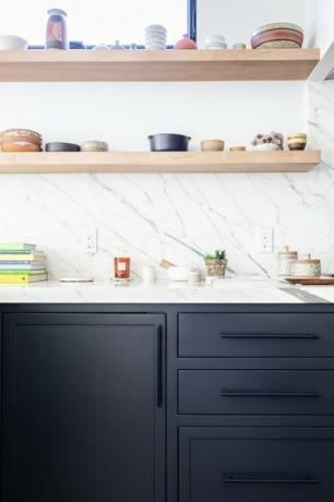 Cocina de paredes blancas con gabinetes de color gris oscuro y estantes de madera con cerámica