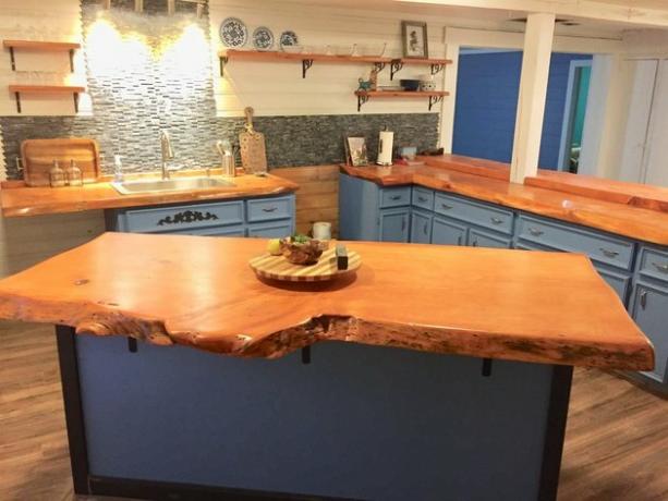 Live-edge houten plaat in moderne keuken met blauwe kasten en houten vloeren