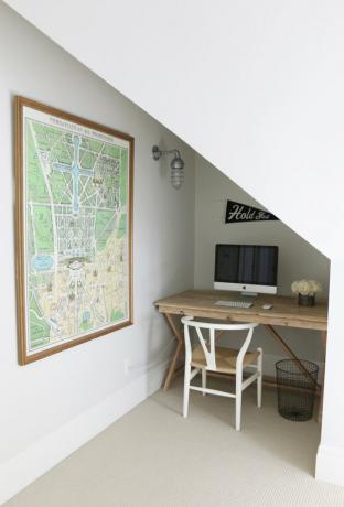 sótão recanto de apartamento com pequena mesa de madeira, cadeira de madeira, computador, mapa na parede.